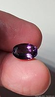 Close-up image of 4.08ct purple amethyst gemstone held between fingers, showing faceted oval shape and deep purple coloration.