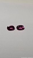 Photo showing two oval-shaped pink-purple Umbalite garnet gemstones on a neutral background, highlighting their matching color and clarity.