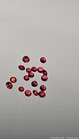 Image showing approximately 18 round cut heated natural rubies in deep red-orange hues scattered on a white background.