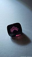 Cushion-cut deep raspberry red to pink spinel gemstone shown with internal reflections and facets.