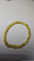 Photo of a stretchy bracelet composed of round lemon yellow jade beads laid flat on a white surface.