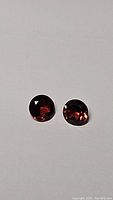 Pair of round deep red Mozambique garnet gemstones on white background showing color and cut.