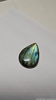 Pear-shaped polished natural labradorite gemstone showing characteristic flash with blue and yellow-green hues.