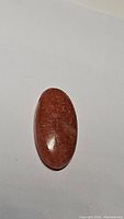 Oval cabochon sunstone showing deep reddish-orange color and surface texture.