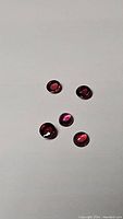 Five small round faceted rhodolite garnet gemstones in pink to purple shades on white background.