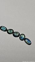 Five oval cut natural sapphires in teal green and blue shades laid out on a flat surface, showing color and clarity
