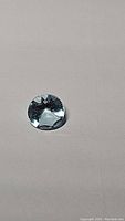 Clear image of a single natural round cut sky blue topaz gemstone on a neutral background showing its color and cut details.