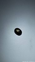 Close-up photo of black star sapphire with visible golden star effect on polished oval cabochon surface.