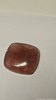 Clear image of natural strawberry quartz cabochon gemstone with a smooth polished surface showing red inclusions.