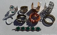 Lot of nine costume jewelry bracelets arranged on a grey surface showing a variety of metal finishes and styles including cuffs, bangles, and stretch bead bracelets.
