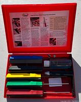 Opened red Gatco plastic case showing multiple colored sharpening stones, rods, and oil bottle with knife sharpening instructions attached to lid.