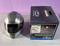 Front view of silver HJC IS-Max motorcycle helmet standing next to its original box labeled with model and size information.