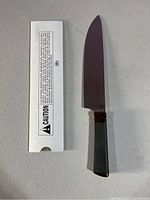 Knife with packaging sleeve laid on flat surface showing the blade and handle with caution label on packaging.