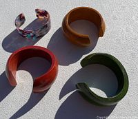 Four colorful open cuff bracelets arranged on a white surface under natural light.