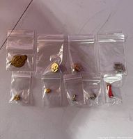 All 9 vintage military pins and medals in clear individual plastic bags displayed on a flat surface.
