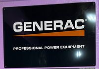 Front view of the Generac metal sign, black background, white and orange logo and text.