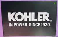 Metal Kohler engine sign with white text on black background, rectangular shape approximately 2x4 feet.