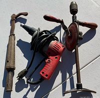 Photo of the three tools: nail puller, red electric drill with cord, and hand crank drill with wooden handles.