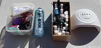 Wide photo showing the nail polish kit components including bottles in a box, a bottle of nail polish remover, and a white nail dryer device.