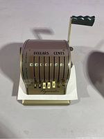 Front angle of Paymaster S-600 manual check printer showing mechanical dials for dollars and cents, numbered sets, lever, and brand name on base
