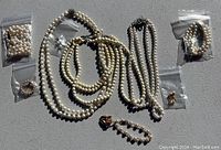 Overview photo showing the two pearl necklaces, two pearl bracelets, pearl earrings, and pearl pin with all items in plastic bags or loose on surface.