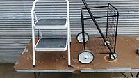Overall view of the metal shopping cart and small step stool on a table showing frames, steps, and wheels.