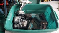 Photo of the green plastic tote containing two cordless drills, reciprocating saw, charger, and batteries, showing overall contents and condition.