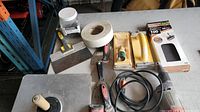 Full view of drywall tools on a table including sanding blocks, mesh tape, putty knives, and mud pan.