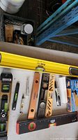 Photo shows a variety of levels including yellow plastic, red plastic, wood with metal components, small green levels, and other related tools laid out on a table.