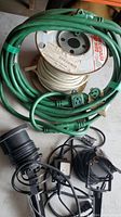 Multiple green plug-in extension cords, partial spool of white electrical wire, two black laser lights with power adapters