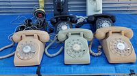 Six rotary dial desk telephones in varied beige and cream tones with cords and visible wear.