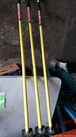 Full view of three yellow quick support rods with black foam handles leaning against a surface.
