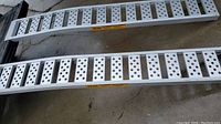 Two aluminum ramps stacked on concrete floor, showing perforated tread design and yellow PRIME labels.