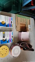 Multiple sandpaper sheets and rolls, boxed sanding sheets and sanding discs for tools on a table.