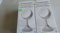 Two boxed Homewerks LED vanity mirrors with Bluetooth speakers, side by side showing front of the packaging.