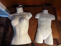Photo showing both white molded half-body mannequins on a table, one adult female torso and one child torso with hooks at the top.