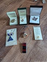 Collection of costume jewelry laid out on wood surface showing various boxed and loose items including brooches, necklaces, pendants, and earrings.