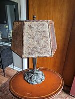 Photo of fiberglass trapezoidal lampshade with textured finish and metal clips on a metal lamp base with floral motifs.
