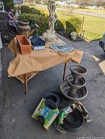 Garden lot items displayed on and around a table outdoors, includes statues, planters, birdhouse, bird feeder, pitcher, and black rubber garden edging rolls on ground.