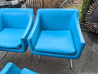 Two blue vintage lounge chairs with boxy design, vinyl torn on cushions, chrome legs with bird feet shape visible