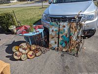 All items displayed outdoors against a vehicle showing canvas flower paintings, metal wall hangings, candle holders on blue stand, and metal stars