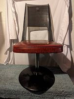 Front view of the black Lucite kitchen chair showing the red padded seat and black swivel base.