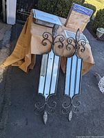 Two large Fleur De Lis style metal mirrors with reflective panels displayed on a table outdoors.