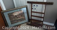 Wall-mounted pool stick holder and large framed picture side by side on floor against wall