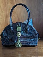 Front view of the dark brown croccodile patterned leather handbag with double handles and decorative medallion charm.