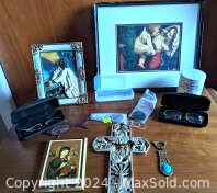 Assortment of religious items on wooden surface including framed hand painted pictures of Jesus and Blessed Mother, eyeglasses and lenses in cases, metal cross, candle holder, and vintage letter opener.