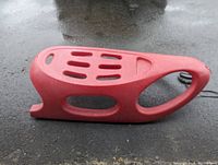 Side view of red plastic sled showing ergonomic seating area and hand grip.