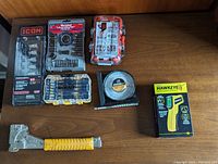 Full set of tools including socket sets, bit sets, stapler, infrared thermometer, and angle locator on wooden surface