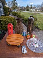 Full lot view on outdoor table showing all items including vases, candle holder, plant base, plastic dishes, wasp traps, and doorbell.