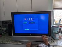 Front view of the TV powered on showing the picture adjust menu on the screen with a blue background. Hand visible adjusting the controls.